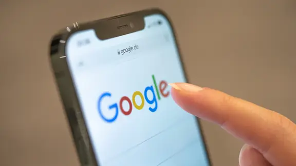 Eine Frau hält ihr Handy in der Hand, auf dem die Google-Seite im Browser zu sehen ist.
